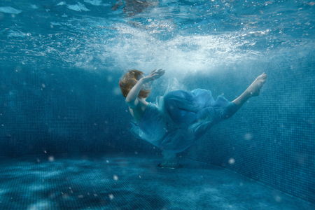 The girl from the fairy tale in a blue dress sinks under water.の写真素材