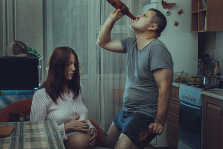 Sad pregnant wife, and next drink alcohol husband. Social problems of the family.の写真素材
