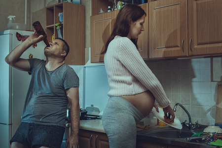 His wife in the kitchen washing dishes, near an alcoholic husband.の写真素材