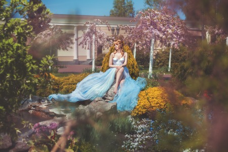 Girl in a long dress sitting among the flowers in the park.の写真素材