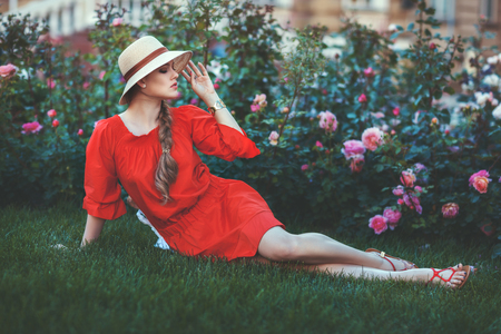 Woman with a hat on his head sitting on the grass in the park on a background of flowers.の写真素材