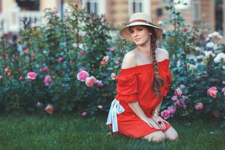 Woman in red dress sitting in the park among the rose bushes.の写真素材