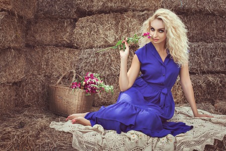 Beautiful blonde woman in the hayloft in the village, she flirts holding a flower.の写真素材