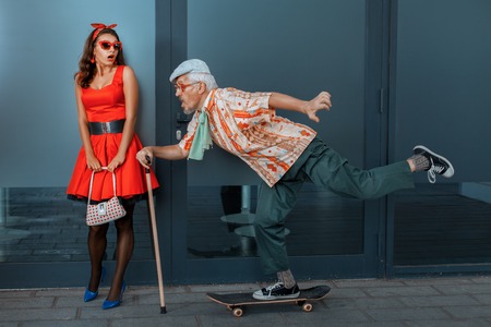 The old man quickly rides on a skateboard on the street, a young girl is surprised.の写真素材