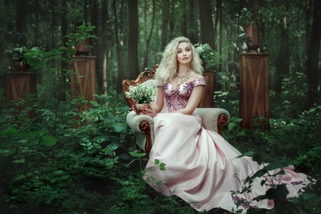 Girl in evening dress sits on a an armchair in the fairy forest.の写真素材