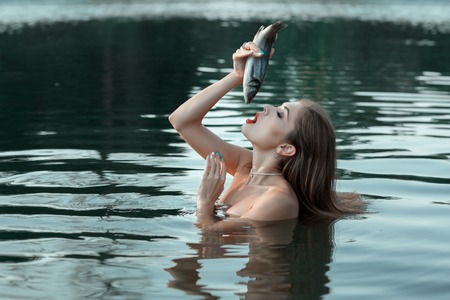 The girl is in the water, she opened her mouth and wants to eat live fish.の写真素材