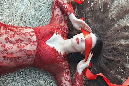 Woman red ribbon covering her eyes, her hair strewn on straw.の写真素材