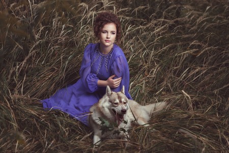 The curly-headed girl dressed in a beautiful dress lies a dog huskies nearby.の写真素材
