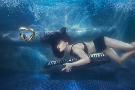 Girl swims with piano under water in the pool.の写真素材