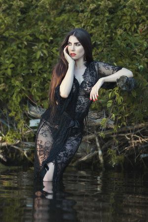 Beautiful thoughtful woman standing knee-deep in water, wearing her peignoir.の写真素材