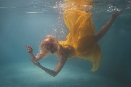 Woman in yellow dress swimming underwater in the pool.の写真素材