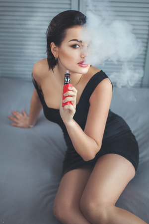 Woman smokes an electronic cigarette and exhales steam out of his mouth.の写真素材