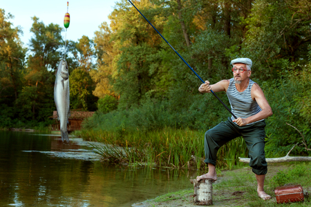 Old grandfather is fishing in the lake in the forest.の写真素材
