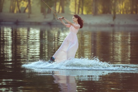 Woman in a dress skates on a lake on a blackboard in the park.の写真素材