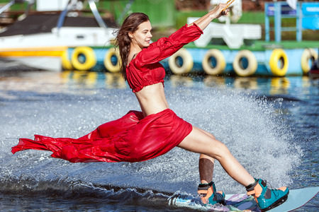 Woman in a red dress does not wakeboard. Her dress is blown by the wind.の写真素材