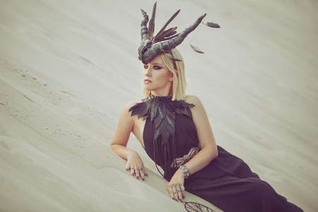 Beautiful woman with animal horns on her head, lying on the sand in the desert.の写真素材