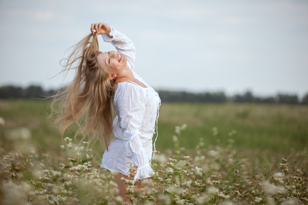 Happy woman is standing in the field and touching her long hair. She is ecstatic about nature.の写真素材