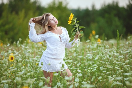 Woman in a field with a sunflower in her hand, she strokes her long hair.の写真素材