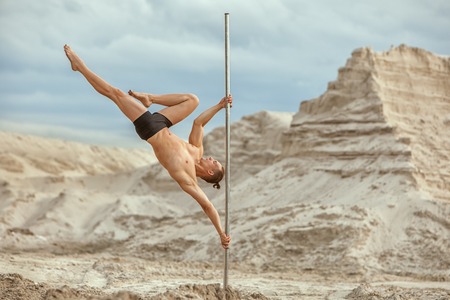 Male gymnast does tricks on a pylon in the desert on the sand.の写真素材