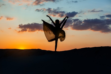 Dancer at sunset against the sky, her dress fluttering. The backlight of the sun only contours of the figures are visible.の写真素材
