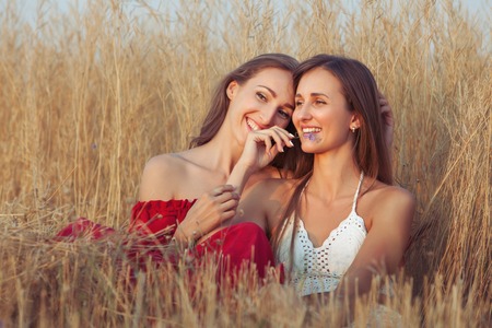 Young women embrace, they sit in the tall grass in the field and smile.の写真素材