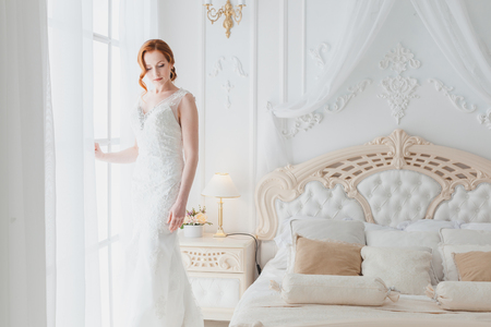 Tender bride in a wedding dress in the bedroom at the window waits for the groom.の写真素材