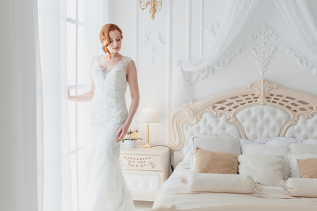 In the bedroom at the window there is a bride in a wedding dress, she worries and is nervous.の写真素材