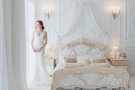 Bride looks out the window at the groom, she is in the bedroom.の写真素材