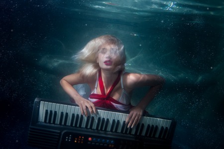 Woman plays music diving under the water, she plays an electric synthesizer.の写真素材