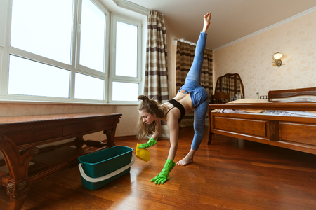 Woman is engaged in fitness during the cleaning in the apartment, she combines sports and chores.の写真素材