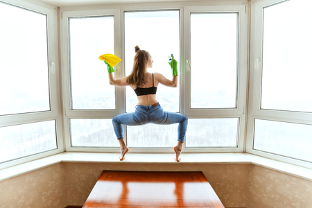Woman washes windows in a yoga pose, she is doing sports while cleaning an apartment.の写真素材