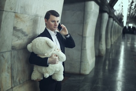 Man is talking on the phone, in his hands a teddy bear is a toy.の写真素材