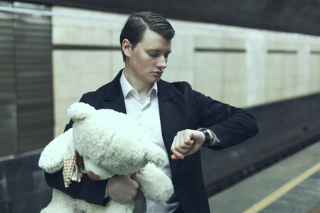 Guy looks at the clock, in his hands the toy is a teddy bear.の写真素材