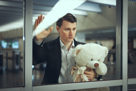 Sad man with a toy bear waiting for a meeting. He looks out the windowの写真素材