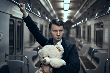 Guy with a teddy bear in the subway. In an empty car he is lonely, it makes him sad.の写真素材
