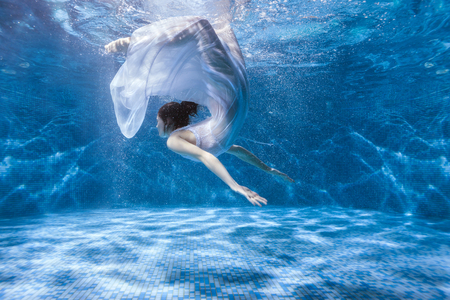 Woman in a white dress dives under the water in the pool.の写真素材