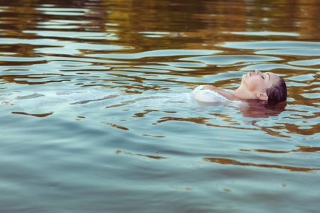 Beautiful woman in a white dress is lying on her back in the water.の写真素材