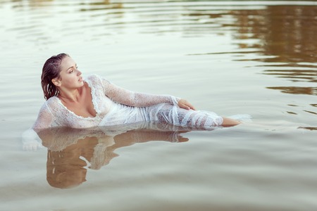 Beautiful woman in white dress lies in the water on the beach.の写真素材