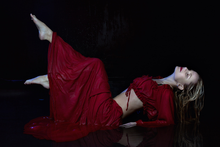 Wet woman in a red dress is lying in the water.の写真素材