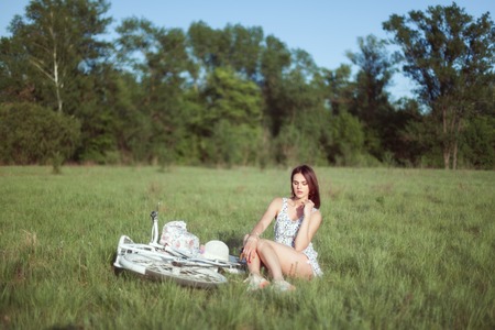Young woman sits in the grass on a meadow. Next to her is her bicycle.の写真素材