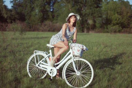 Portrait of a beautiful young woman in a meadow. She sits on a white bicycle.の写真素材
