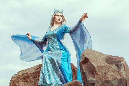 Beautiful elf woman in blue dress sits on top of a mountain.の写真素材
