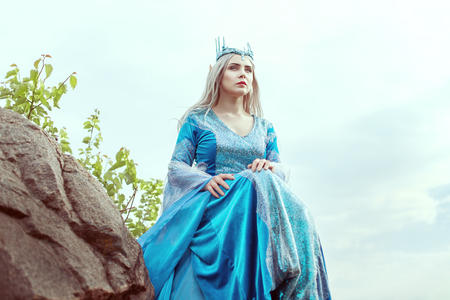 Beautiful elf woman in a blue dress is sitting on the mountain.の写真素材
