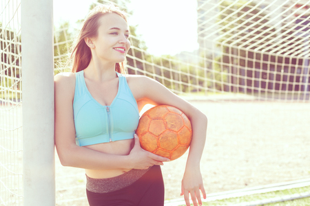 On the football field a woman in her arms holds a soccer ball.の写真素材