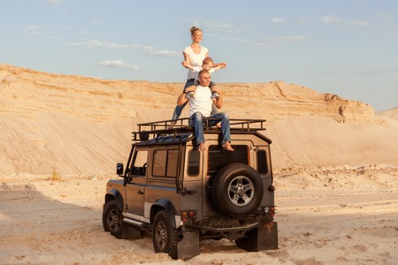 Young family with a child are sitting on the roof of a car in the desert.の写真素材
