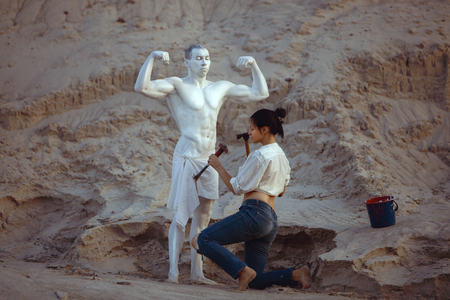 Woman carves a figure of a sports man from a stone. Sculpture of a man with a beautiful body.の写真素材