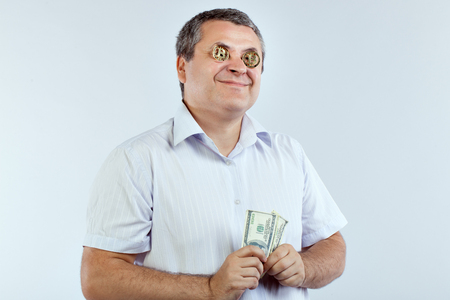 Businessman with bitcoins in his eyes smiles. He's holding dollars in his hands.の写真素材