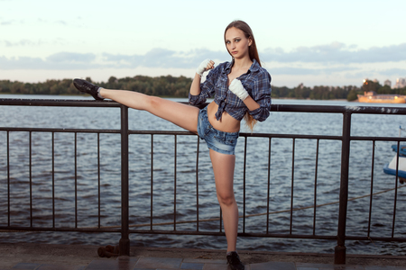 Young woman fighter doing sports stretching on the river bank.の写真素材