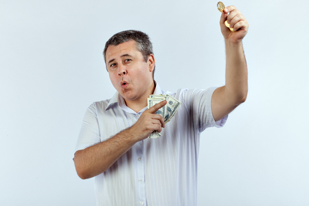 Man points to the bitcoin, holding dollars in his hand.の写真素材