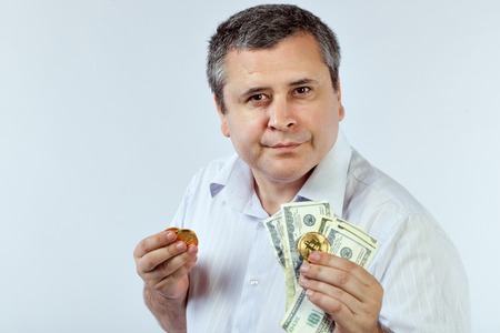 Man in a white shirt holding a coin Bitcoins and dollars.の写真素材
